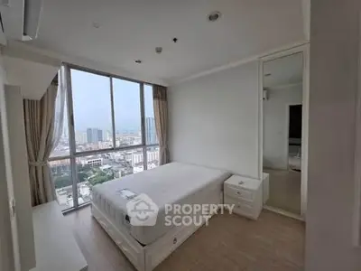 Spacious bedroom with large window offering stunning city views in modern apartment.