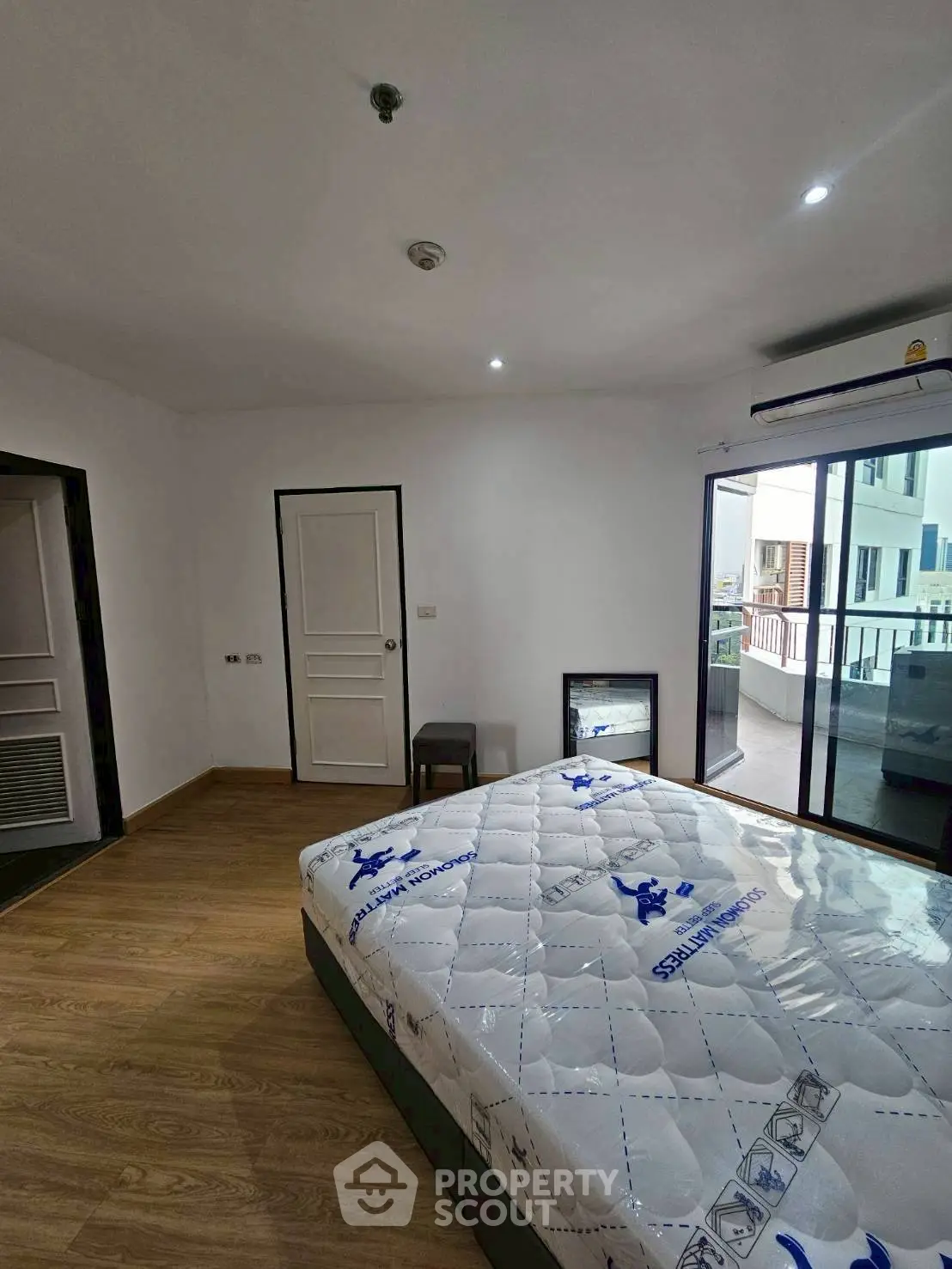 Spacious bedroom with balcony access and natural light, featuring a comfortable mattress and modern decor.