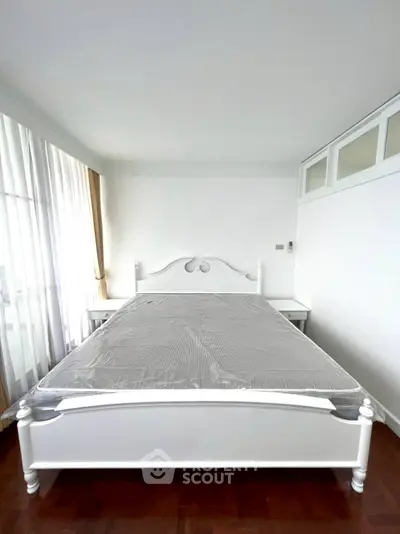 Spacious bedroom with elegant white bed and natural light from large windows.