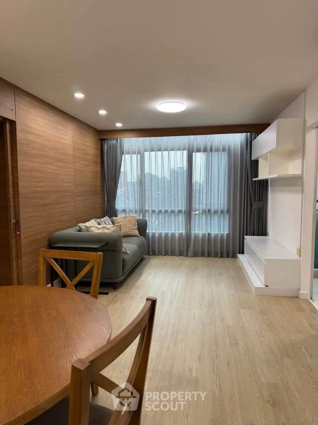Modern living room with wooden flooring and large window, featuring a cozy sofa and dining area.