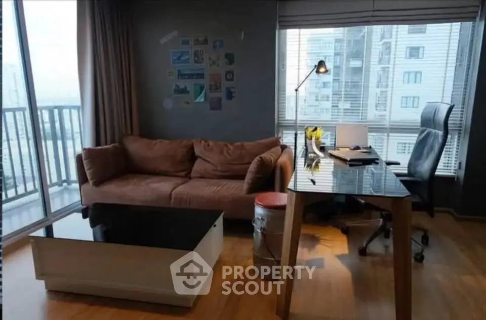 Modern living room with city view, featuring a cozy sofa, sleek desk, and large windows for natural light.