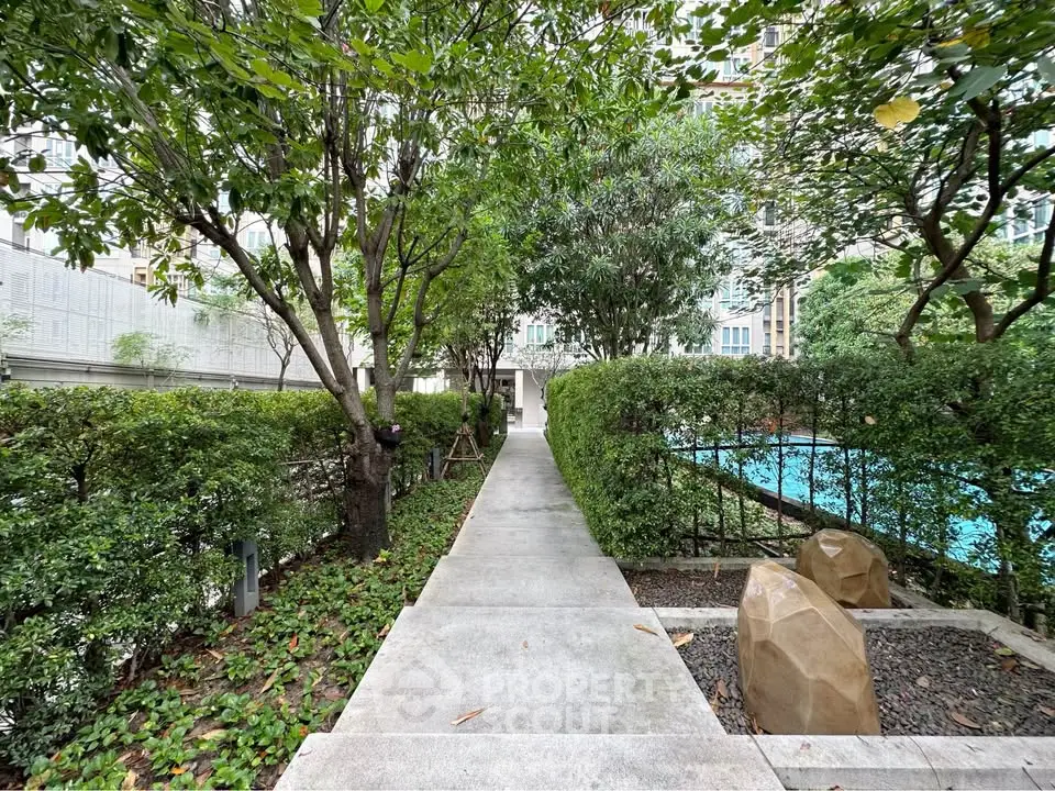 Lush garden pathway leading to a serene pool in a modern residential complex.