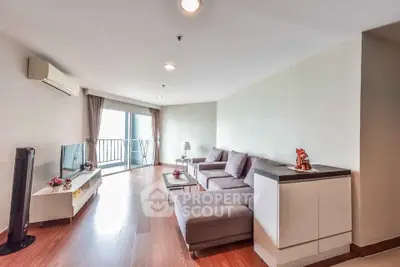 Spacious modern living room with large windows and balcony access, featuring stylish furniture and wooden flooring.