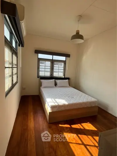 Spacious bedroom with wooden flooring and large windows for natural light.