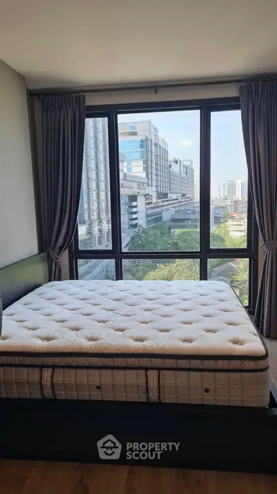 Spacious bedroom with large window offering stunning city view in modern apartment.