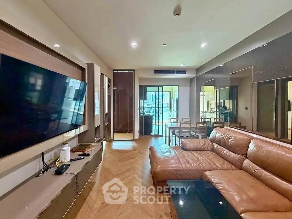 Spacious modern living room with leather sofa and large TV, featuring elegant wooden flooring and ample natural light.