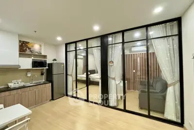 Modern open-layout apartment with glass partition, featuring a compact kitchen and cozy living area.