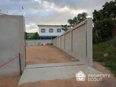 Spacious driveway leading to a modern two-story home with vibrant window accents, surrounded by a high privacy wall and lush greenery.