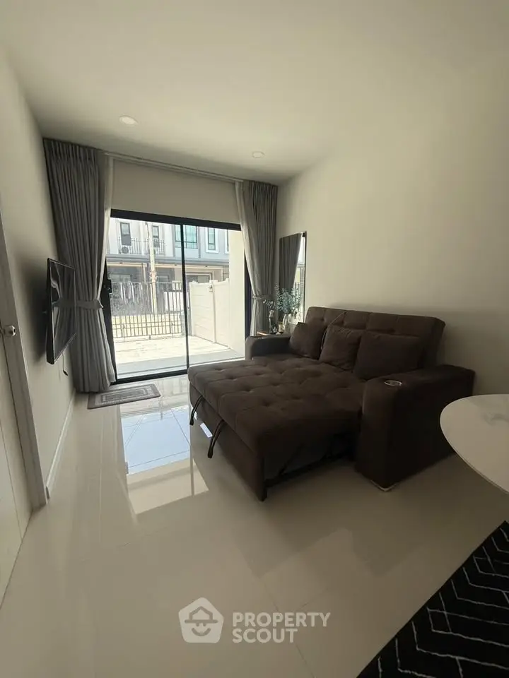 Modern living room with sleek sofa and large window offering natural light and outdoor view.