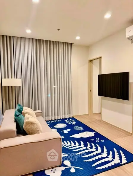 Modern living room with stylish decor and wall-mounted TV, featuring a cozy sofa and vibrant blue rug.