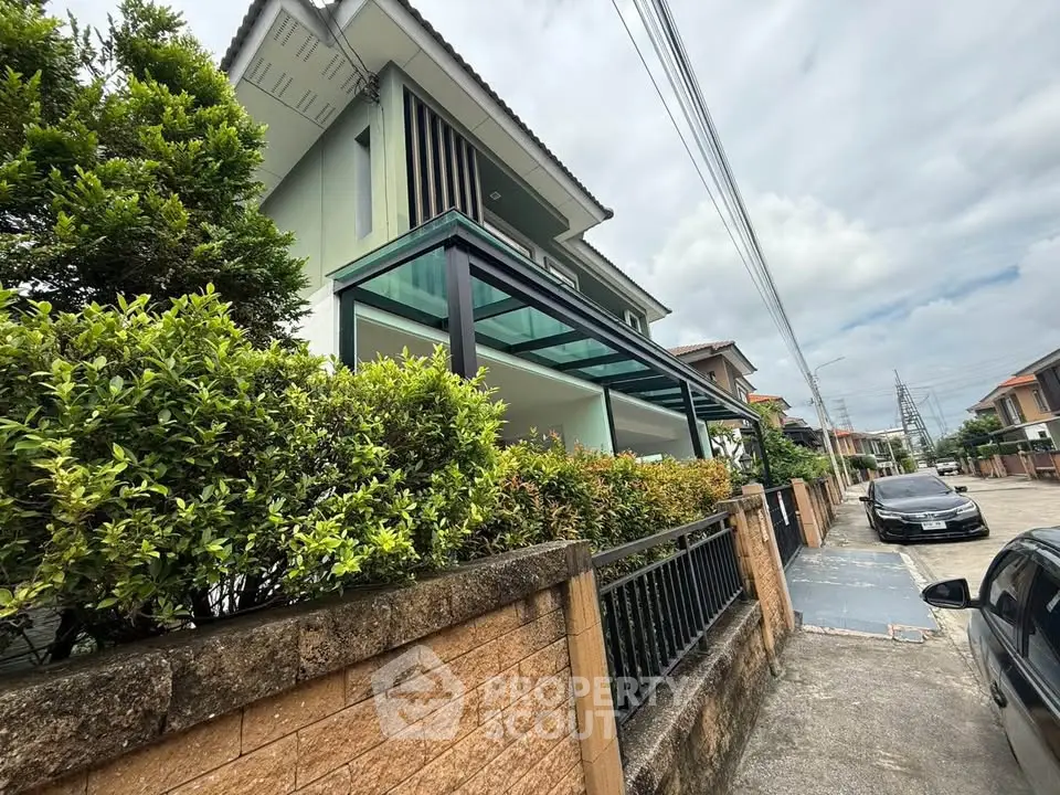 Modern two-story house with lush greenery and a sleek glass balcony in a suburban neighborhood.