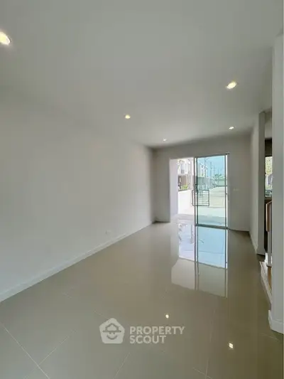 Spacious modern living room with glossy tiled floors and large glass doors leading to a balcony.