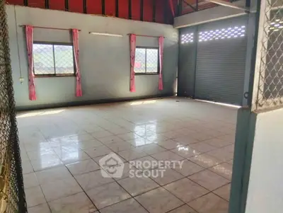 Spacious tiled room with large windows and roller shutter, ideal for versatile use.