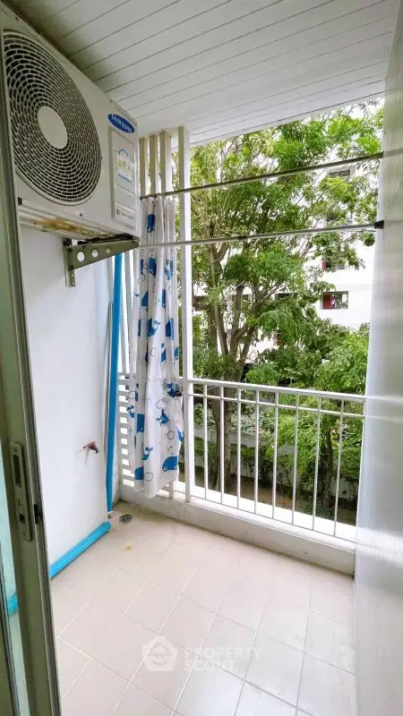 Charming balcony with lush green view and air conditioning unit, perfect for relaxation.
