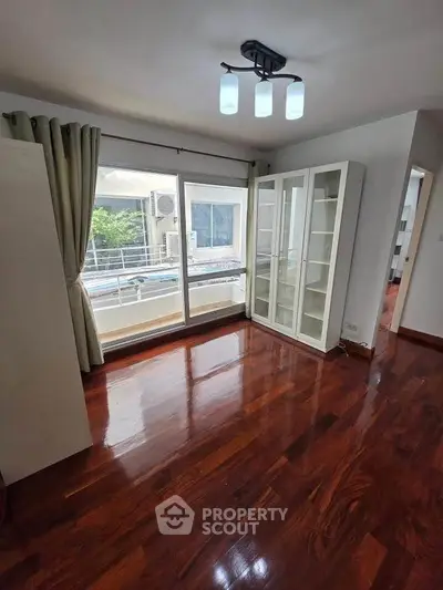 Spacious room with polished wooden floors and large window in modern apartment.