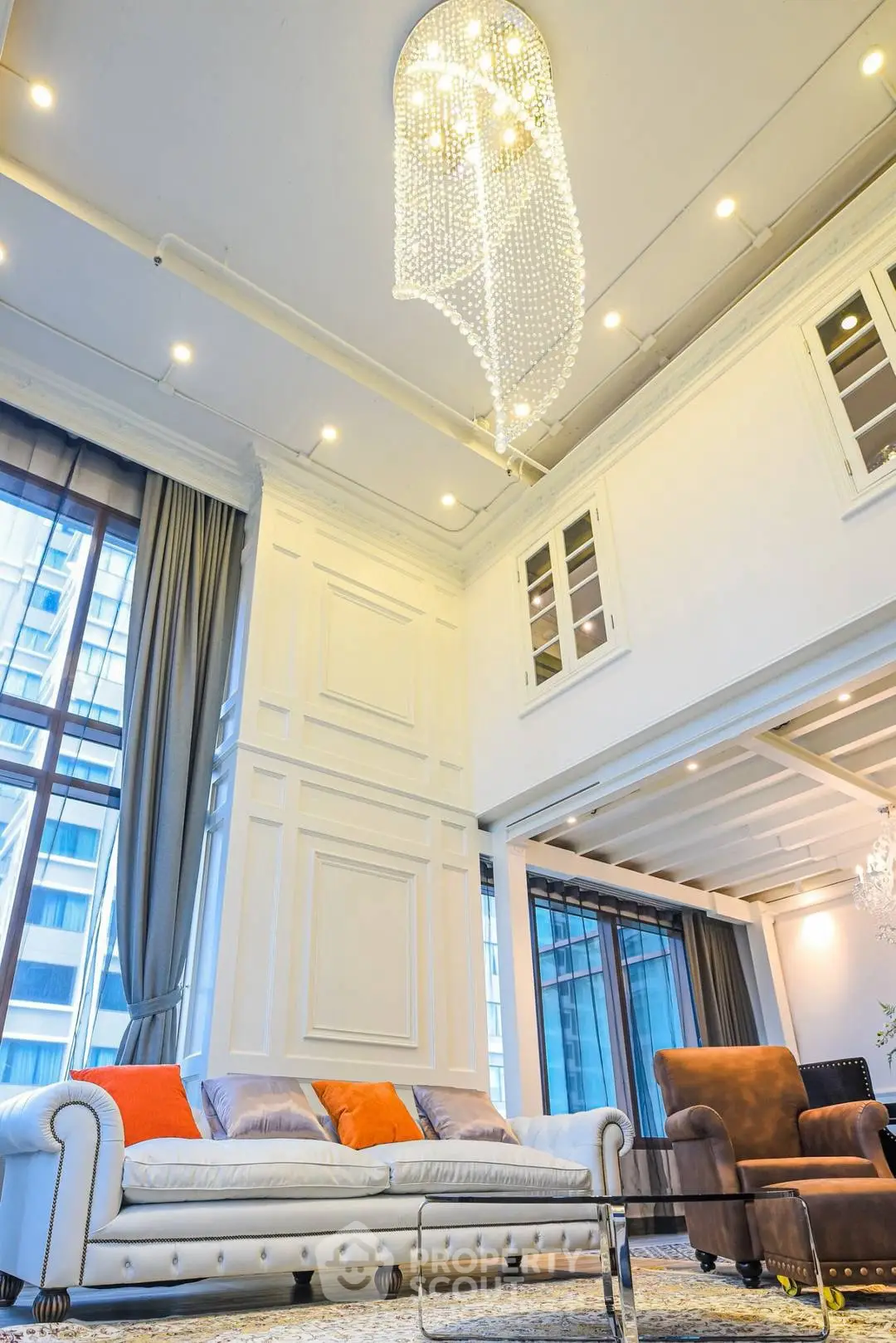 Luxurious living room with high ceilings, elegant chandelier, and large windows offering city views.