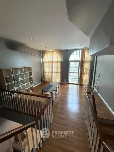 Spacious modern living room with high ceilings and large windows, featuring wooden flooring and minimalist decor.