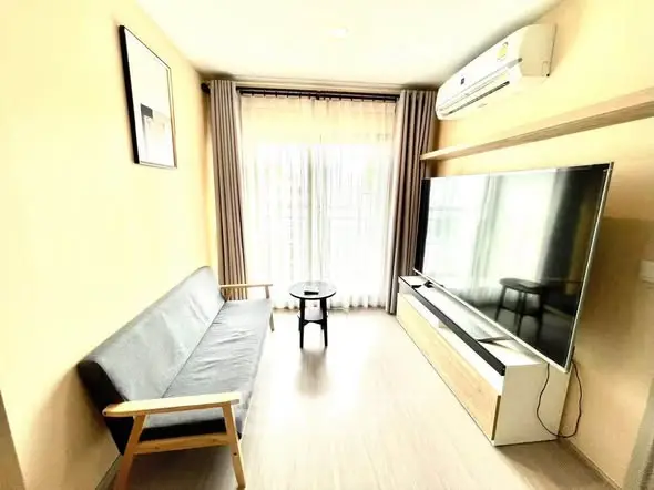 Modern living room with large TV and stylish sofa, featuring natural light from floor-to-ceiling windows.