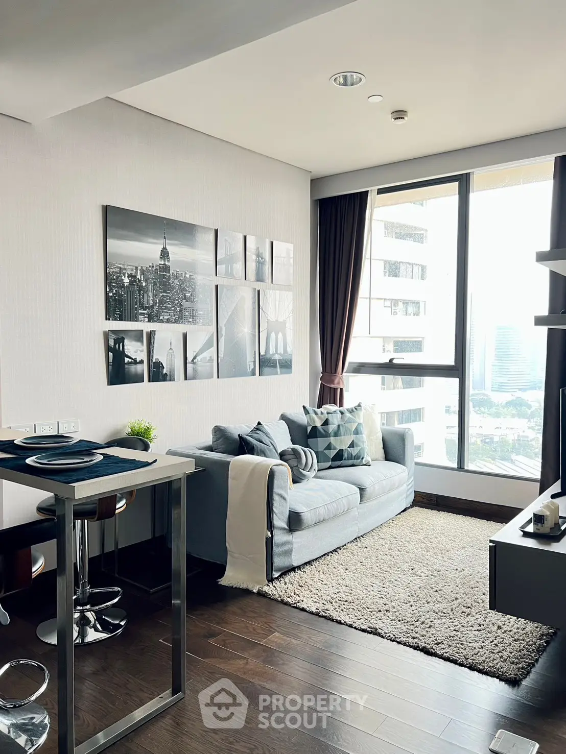 Modern living room with city view, stylish decor, and cozy seating area in a high-rise apartment.