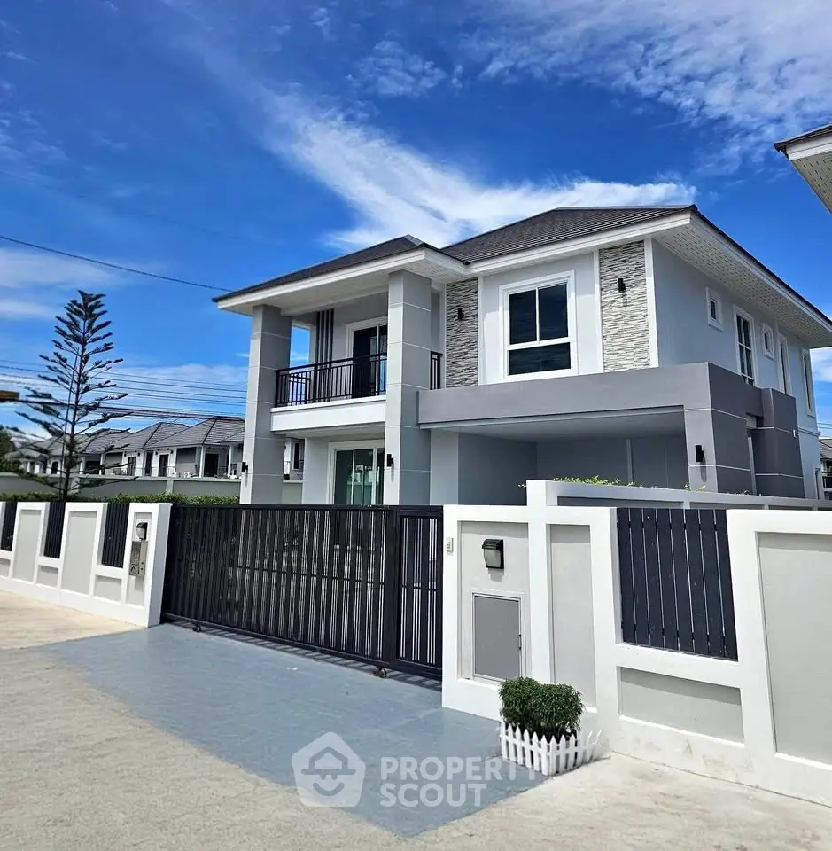 Modern two-story house with sleek design and gated entrance under a clear blue sky.