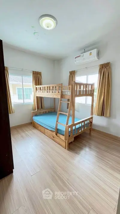 Bright bedroom with bunk bed and air conditioning, featuring wooden flooring and large windows.