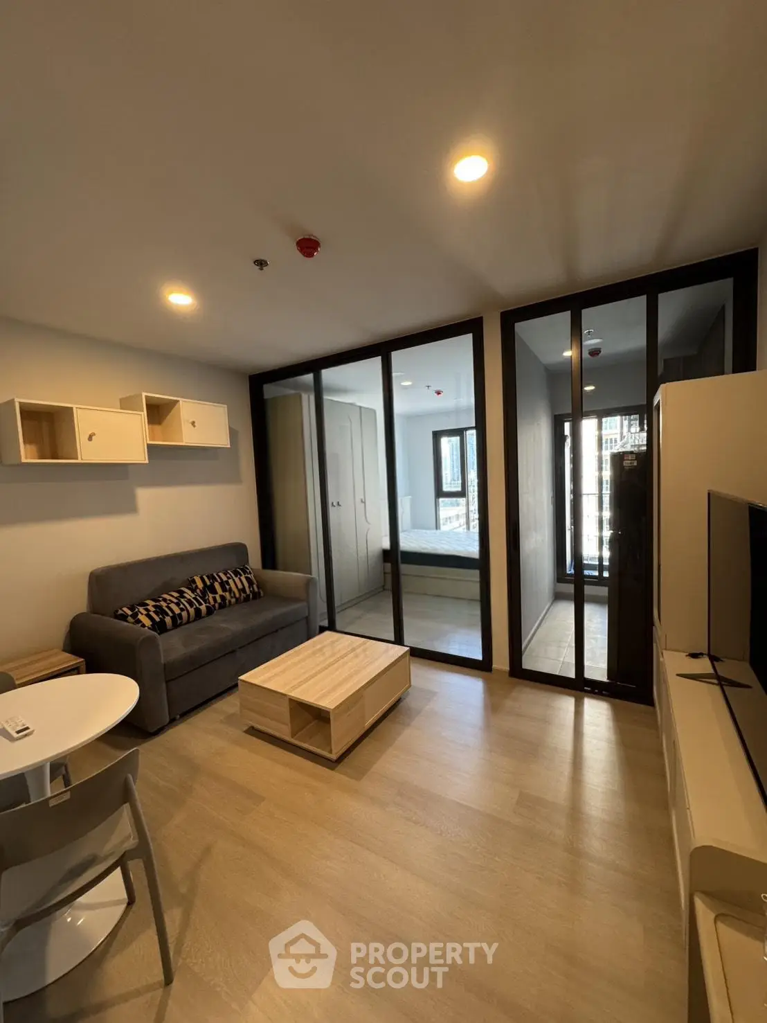 Modern living room with stylish furniture and glass partition leading to bedroom