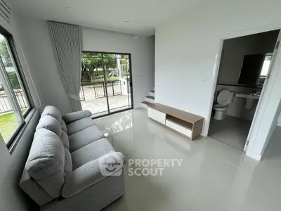 Modern living room with gray sofa, large windows, and view of outdoor greenery.