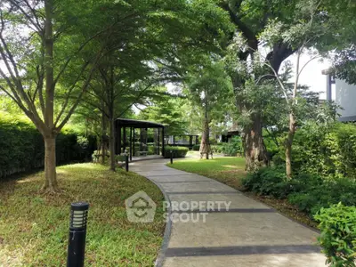Serene garden pathway with lush greenery and shaded seating area in a residential complex.