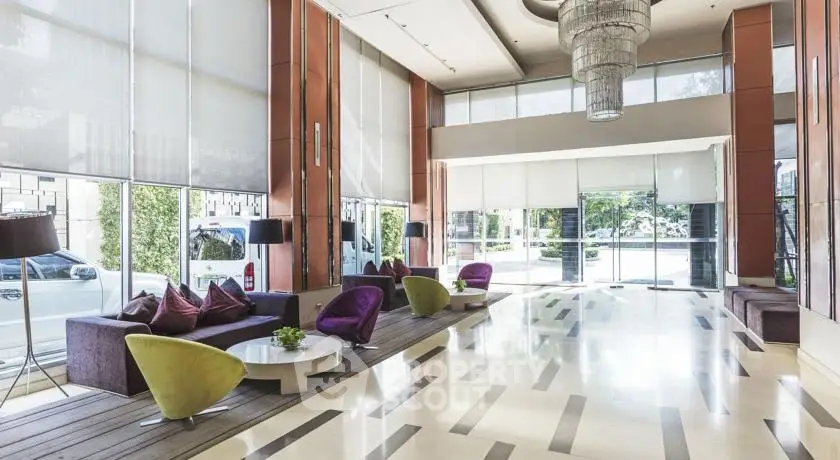 Luxurious modern lobby with stylish seating and grand chandelier in upscale building.