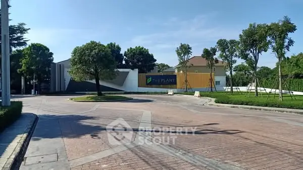 Modern residential entrance with lush greenery and clear blue sky.