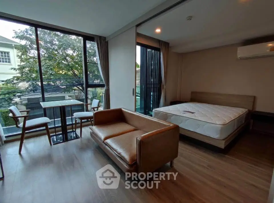 Spacious studio apartment with large windows and modern furnishings, offering a cozy living and sleeping area.