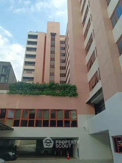 Modern multi-story building with parking area and lush greenery on facade.