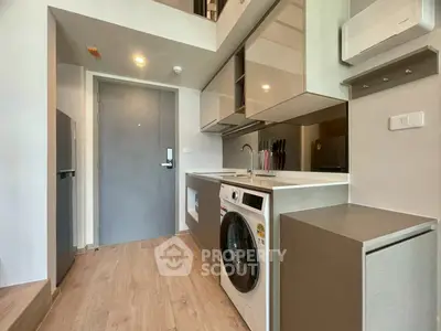 Modern kitchen with washing machine and sleek cabinetry in compact apartment