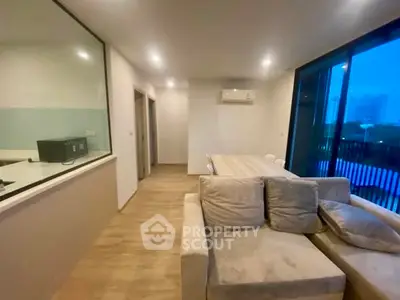 Modern living room with cozy sofa and dining area, featuring large windows and wooden flooring.