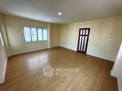 Spacious empty room with wooden flooring and large windows, perfect for customization.