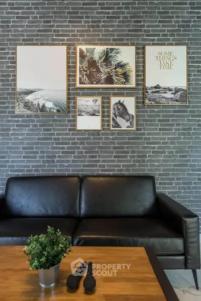 Stylish living room with black leather sofa, brick wall, and framed art decor.