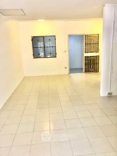 Spacious tiled room with barred window and decorative door, ideal for versatile use.