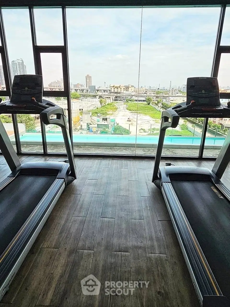 Modern gym with treadmills and panoramic city view through large windows.