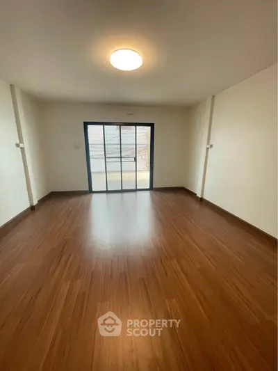 Spacious empty room with wooden flooring and large window, perfect for customization.