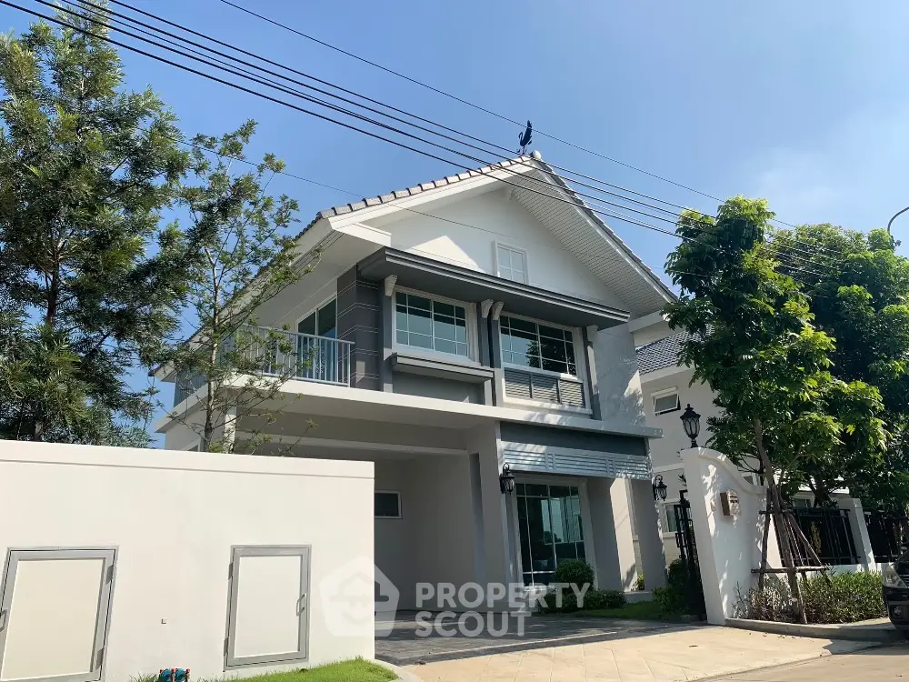 Modern two-story house with large windows and lush greenery in a serene neighborhood.