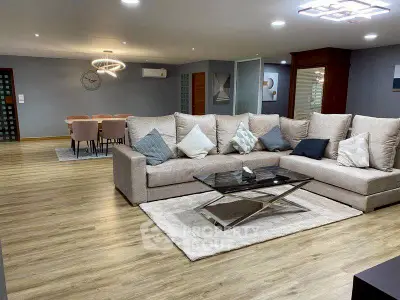 Spacious modern living room with elegant decor and open dining area, featuring a large sectional sofa and stylish lighting.
