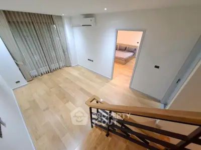 Spacious modern living area with wooden flooring and staircase, leading to a cozy bedroom.