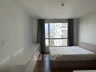 Spacious bedroom with large window and modern furnishings in a high-rise apartment.