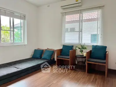 Cozy living room with wooden flooring, modern seating, and natural light from large windows.