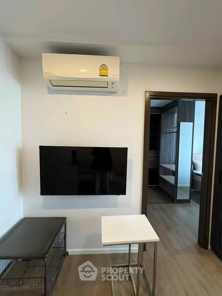 Modern living room with wall-mounted TV and air conditioning, featuring sleek furniture and wooden flooring.