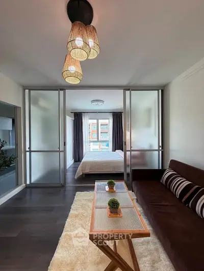 Modern living room with stylish decor and view into a cozy bedroom through sliding glass doors.