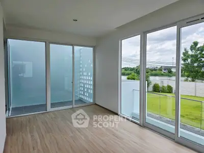 Spacious modern room with large windows and balcony overlooking lush greenery.