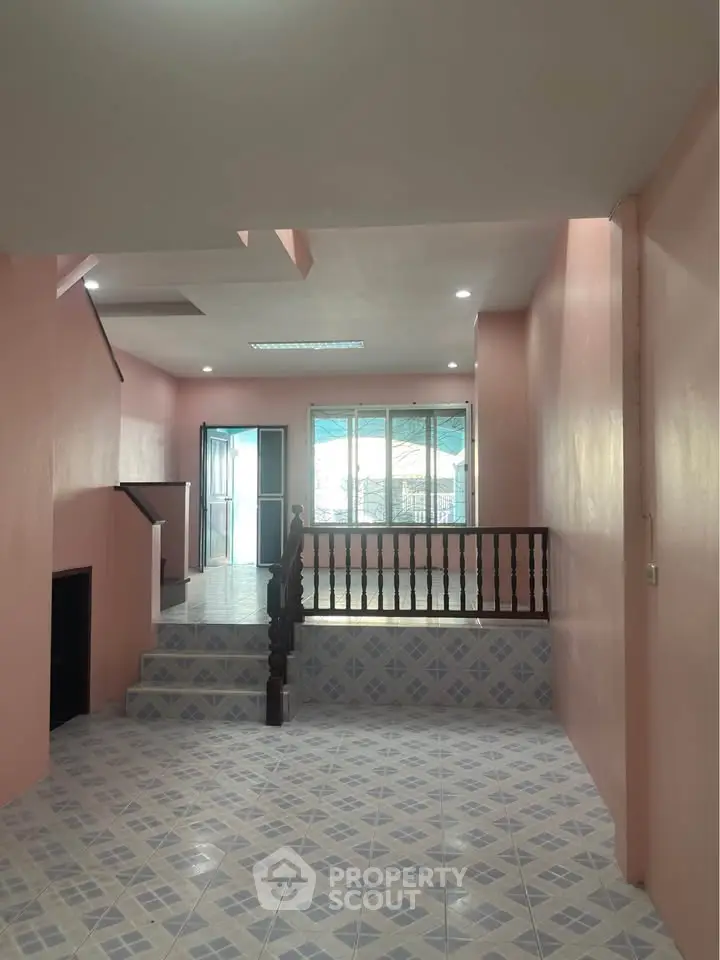 Spacious multi-level interior with pink walls and tiled flooring, featuring large windows for natural light.