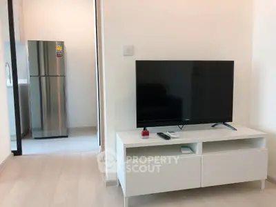 Modern living room with sleek TV stand and view into a contemporary kitchen with stainless steel fridge.