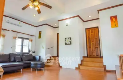 Spacious living room with modern decor and wooden flooring, featuring a cozy seating area and ceiling fan.